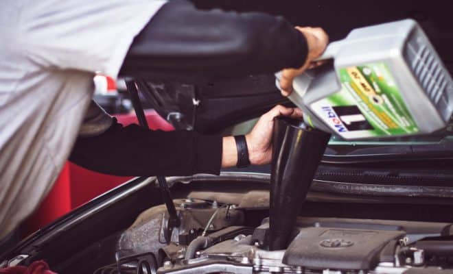 man refilling motor oil on car engine bay